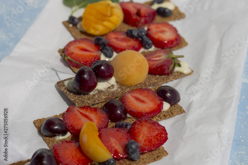 Healthy and tasty toasts with curd cheese  fruits and berries on a white parchment paper.