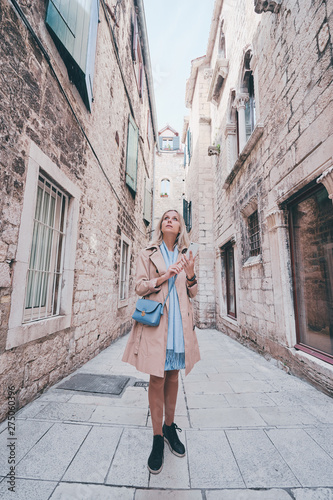 Travel and technology. Happy young woman in coat using smartphone walking by Split Old Town.