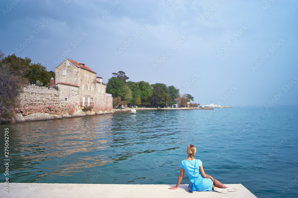 Tourism concept. Young traveling woman enjoying the view of Kastel Castle sitting near the sea on Croatian coast. Tourism concept. Young traveling woman enjoying the view of Kastel Castle sitting near the sea on Croatian coast.