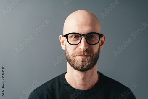 Young smiling man with beard and glasses on gray studio background