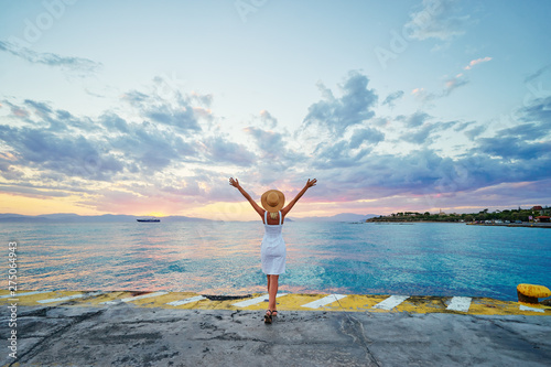Traveling by Greece. Young happy woman rising hands up enjoying beautiful sunset on the sea.