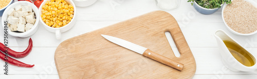 top view of wooden chopping board with knife on white table, panoramic shot