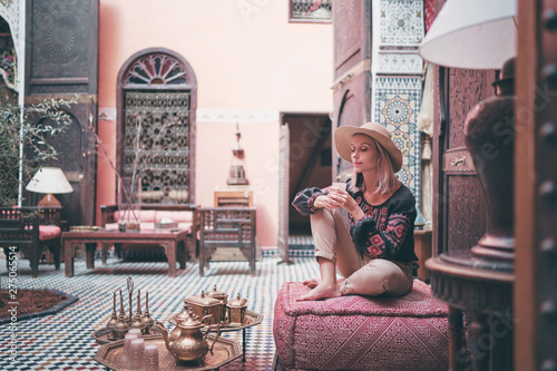 Traveling by Morocco. Happy young woman in hat relaxing in traditional riad interior in medina. photo