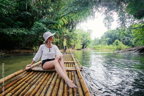 Traveling by Thailand. Pretty young woman enjoying view sailing jungle river on traditional bamboo raft.