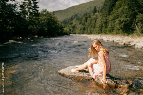 Caucasian young girl posing at stone in the river in summer day.
