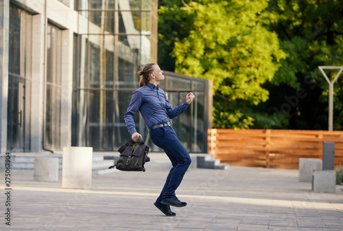Crazy young businessman dancing on the street with bag. Celebrating victory. Flexibility and grace in business