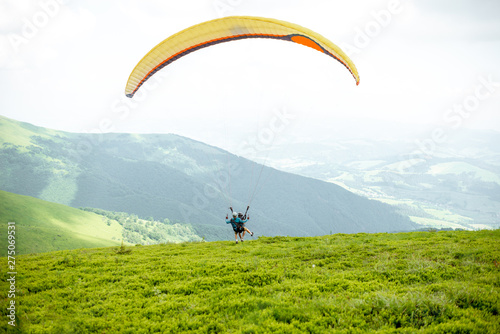 Men starting a paraglider flight, running on the green meadow high in the mountains