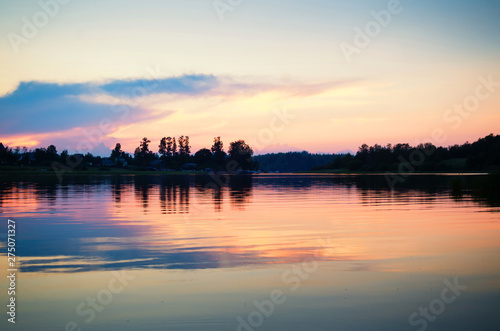 Beautiful golden sunset on a lake. Black silhouetter of trees on the lake shore. Peaceful time at dusk.