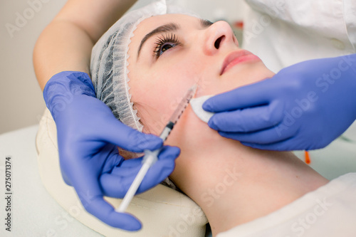 The doctor cosmetologist makes the Botulinotoxin injection procedure for tightening and smoothing wrinkles on the face skin of a beautiful  young woman in a beauty salon.Cosmetology skin care.