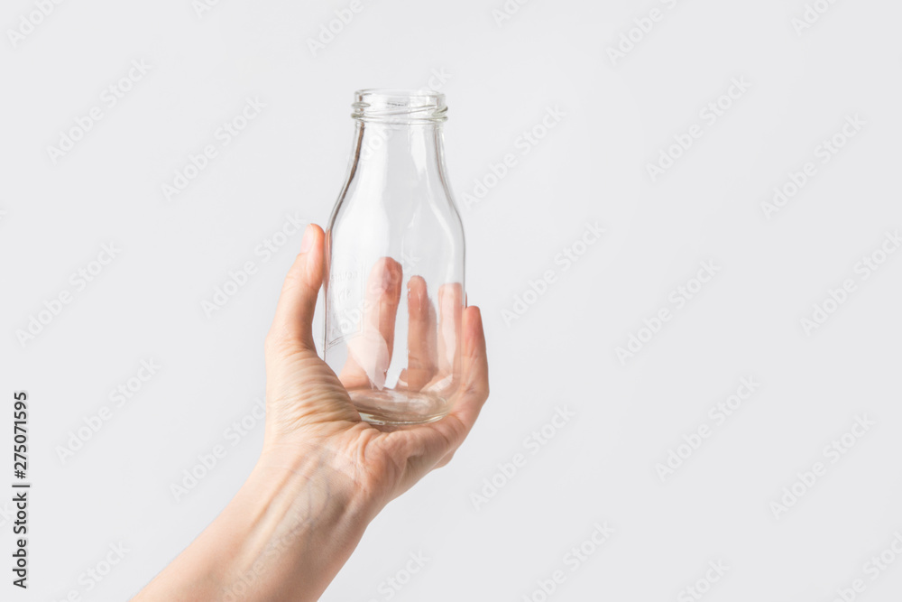 Young caucasian woman holds in hand empty glass bottle on white wall background. Reusable materials plastic-free alternatives zero waste environmental protection food storage concept