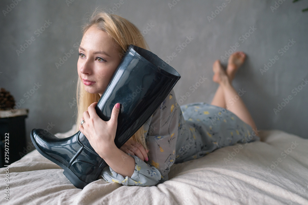 Strange woman hugs rubber boot on bed. - obrazy, fototapety, plakaty 