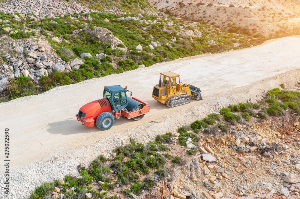 Roller and excavator on a dirt road before laying asphalt, aerial view. Roller and excavator on a dirt road before laying asphalt, aerial view.
