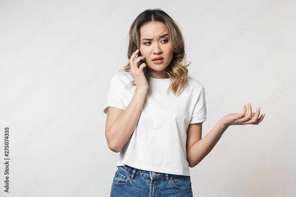Shocked emotional young woman posing isolated over white wall background talking by mobile phone. Shocked emotional young woman posing isolated over white wall background talking by mobile phone.