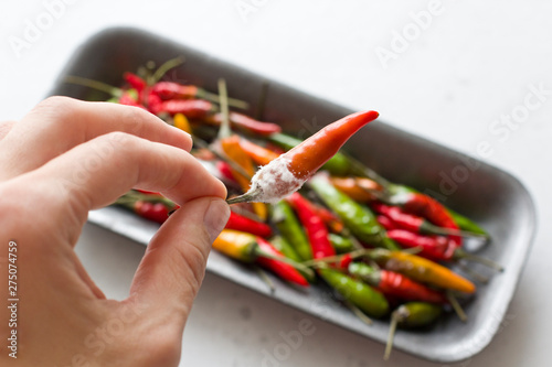 White mold on orange chili peppers, on a modern light gray background. Spoiled food, vegetables. Hand holds chili pepper photo