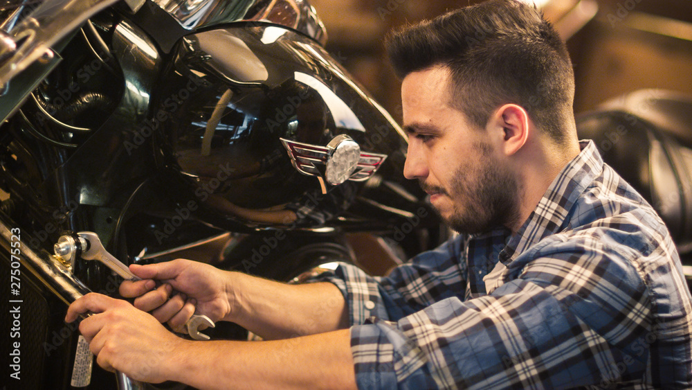 Obraz premium Man is tightening nuts with a spanner and repairing his motorcycle in a garage.