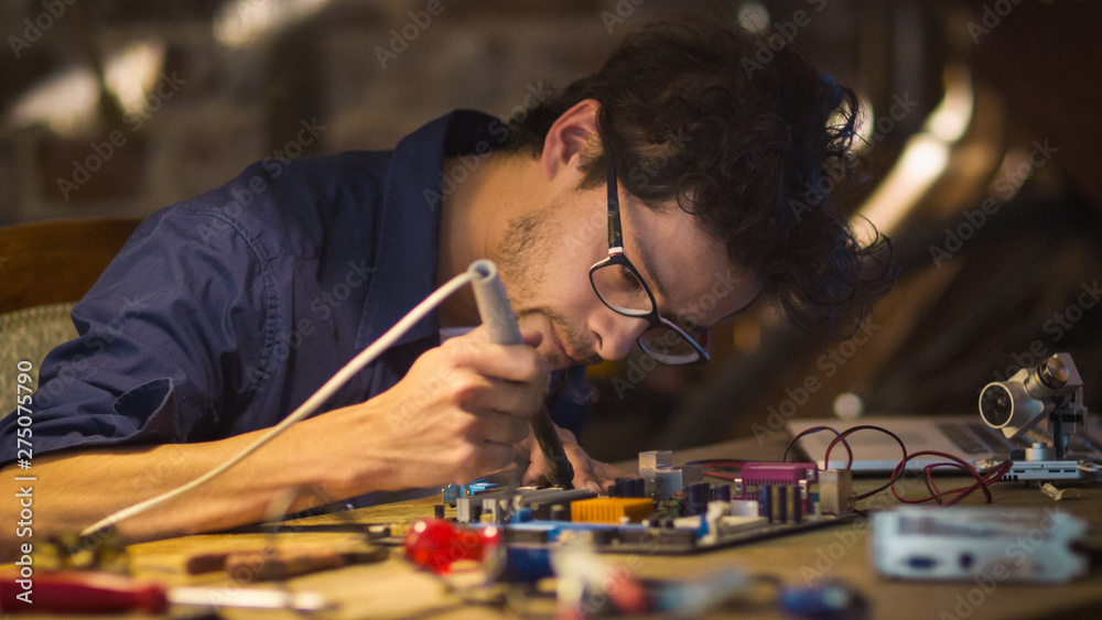 Student is studying electronics and soldering a circuit board in a garage. - obrazy, fototapety, plakaty 