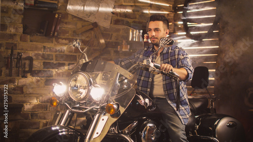 Man started his motorcycle and revs engine in a garage. He is sitting on his Chopper Motorbike. photo