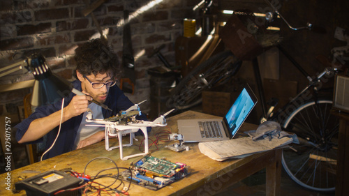 Fototapeta Naklejka Na Ścianę i Meble -  Student is soldering electrical components on a drone in a garage while checking a laptop computer.