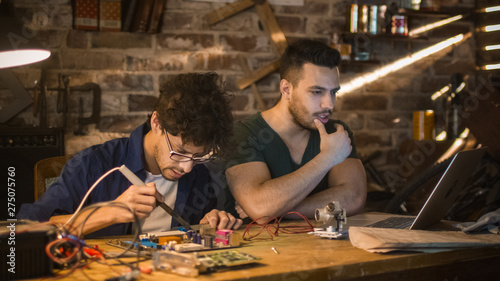 Two students are studying electronics and soldering in a garage.