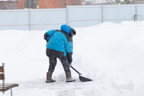 Old woman in warm blue jacket clears a snowdrifts with a snow shovel