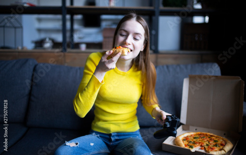 Funny brunette girl in yellow sweater eating pizza at home
