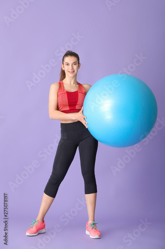 Young sporty woman with fitball on color background