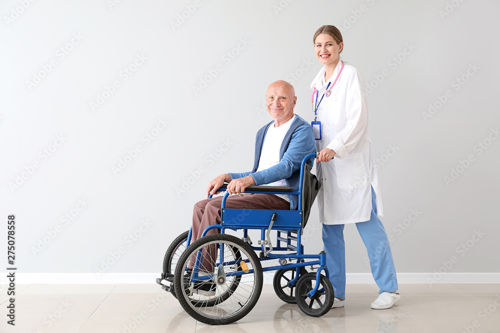 Elderly man in wheelchair and doctor near light wall Elderly man in wheelchair and doctor near light wall