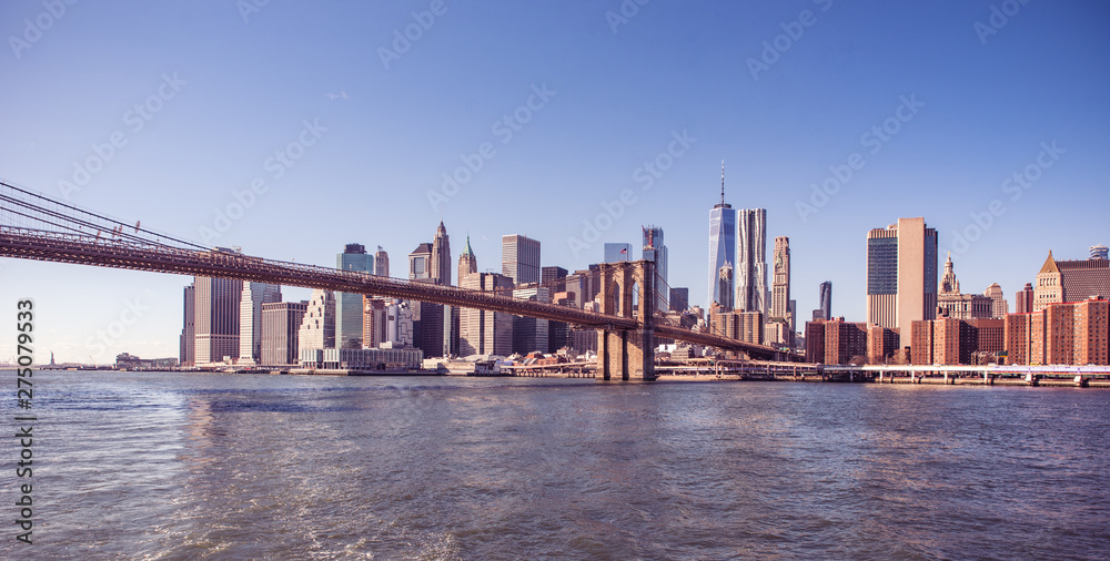 Naklejka premium Famous Skyline of downtown New York City, Brooklin Bridge and Manhattan with skyscrapers illuminated over East River panorama. New York, USA