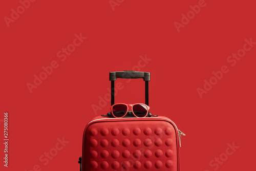 red colorful textured travel bag with sunglasses isolated on red