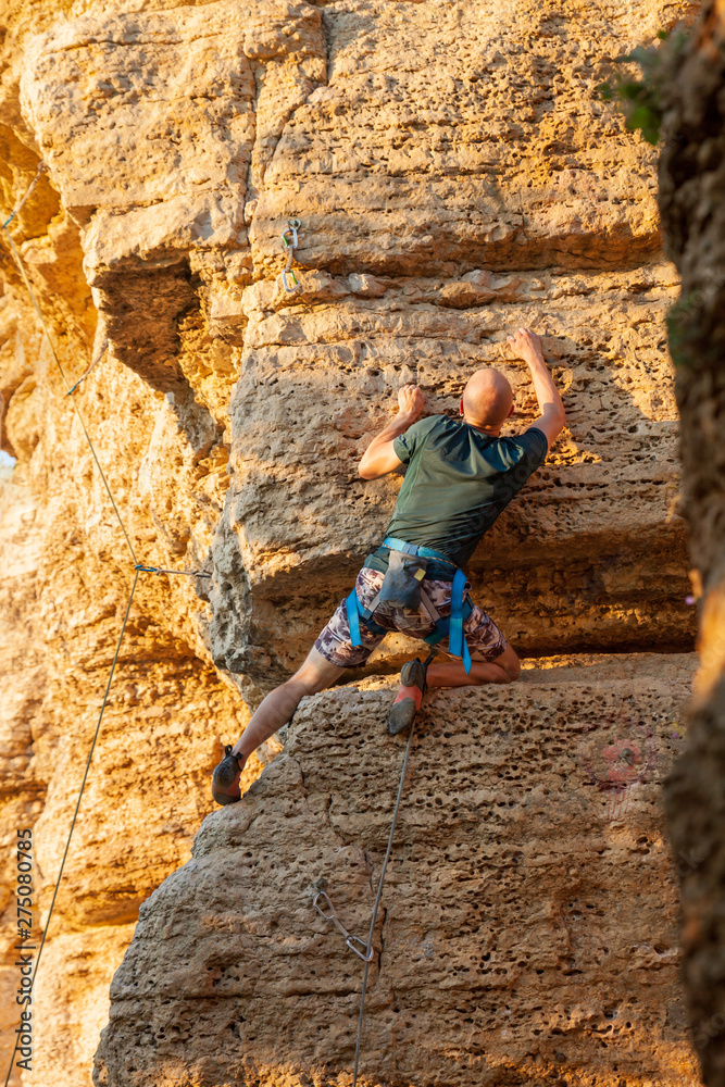 Climber man climbs cliff or mountain on the sunset