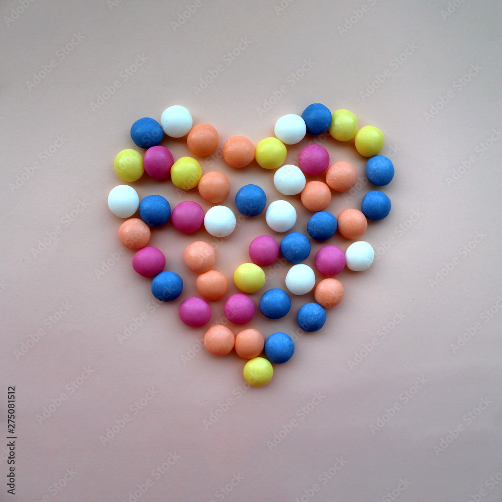 Heart shape made with small multicolored round candies laying in the middle peach background. Wedding invitation template Heart shape made with small multicolored round candies laying in the middle peach background. Wedding invitation template