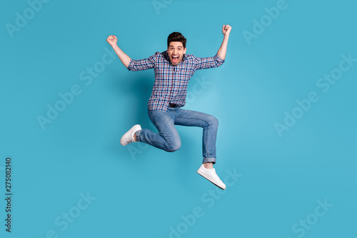 Full length body size view photo cute nice youth raise fists scream yeah celebration wonderful news thrilled satisfied candid checked shirt jeans sneakers weekend holidays isolated blue background