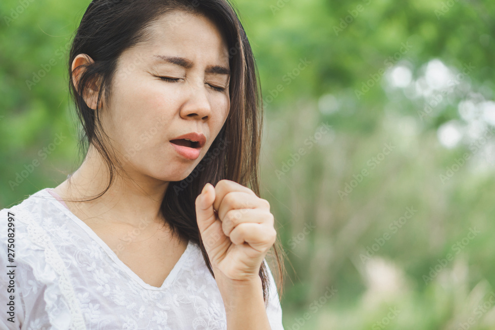 sick Asian woman feeling unwell and coughing outdoors in a park sick Asian woman feeling unwell and coughing outdoors in a park
