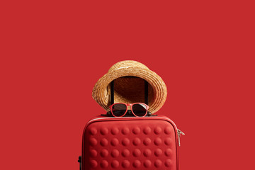 red colorful travel bag with straw hat and sunglasses isolated on red
