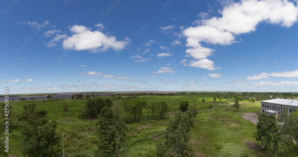 Beautiful landscape of green valley with some trees, deep blue sky with white clouds and small brick house from side