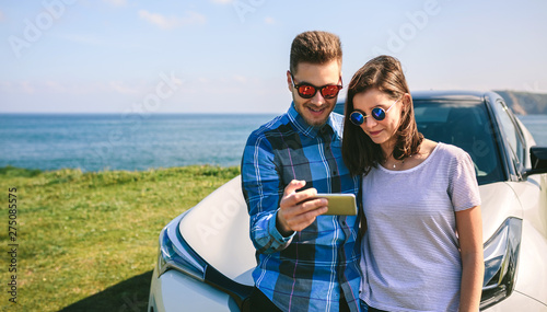 Young couple traveling by car making a stop and looking the mobile