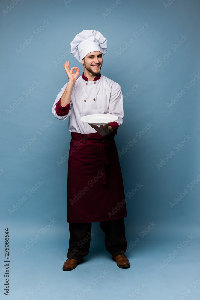 Positive professional happy man chef showing tasty ok sign isolated on light blue. Positive professional happy man chef showing tasty ok sign isolated on light blue.