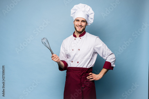 Portrait of positive toothy chef cook in beret, white outfit having tools in crossed arms looking at camera.