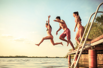 A group of young people joyfully leap into the refreshing lake waters on a sunny summer day, embracing the carefree moments of pure fun and laughter.