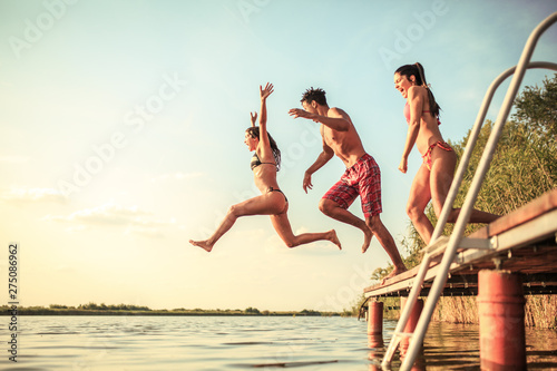 A group of young people joyfully leap into the refreshing lake waters on a sunny summer day, embracing the carefree moments of pure fun and laughter.