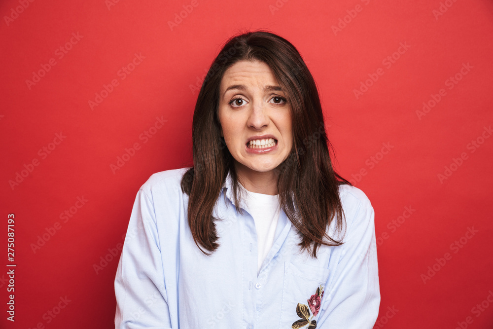 Fototapeta premium Amazing confused young beautiful woman posing isolated over red wall background.