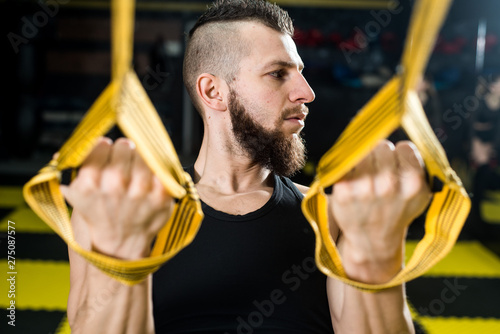 Muscular man does crossfit with TRX fitness straps in the gym with black and yellow interior