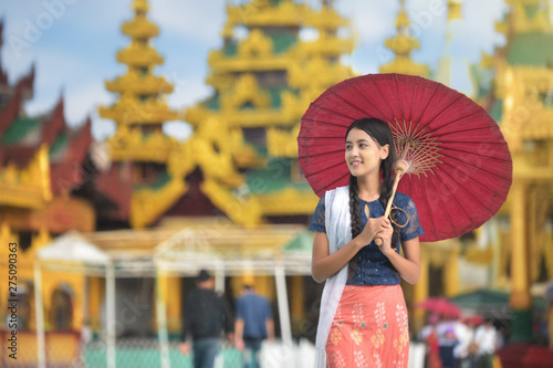 Burmese girl holding a red umbrella walking at Shwedagon Pagoda. Young Myanmar girls with Thanaka, a yellowish-white paste made from ground bark and used as a cosmetic and for sunburn.