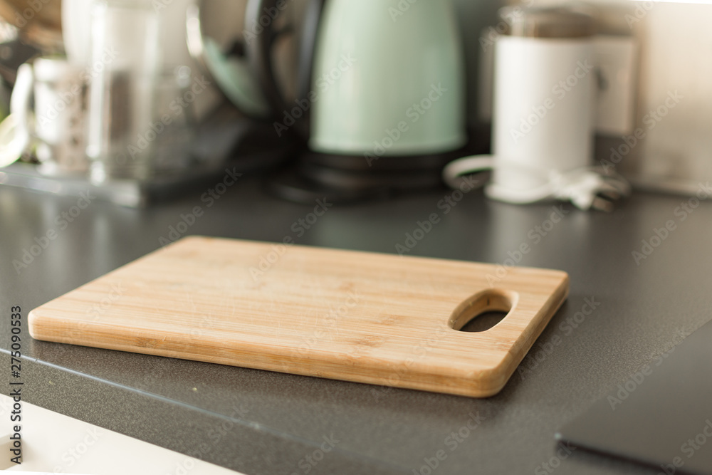Empty wooden cutting board on the kitchen table interior. Cutting bamboo board on blurred kitchen indoors background. Template for design.