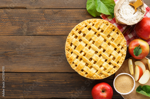 Apple pie with lattice top and ingredients on wooden table.