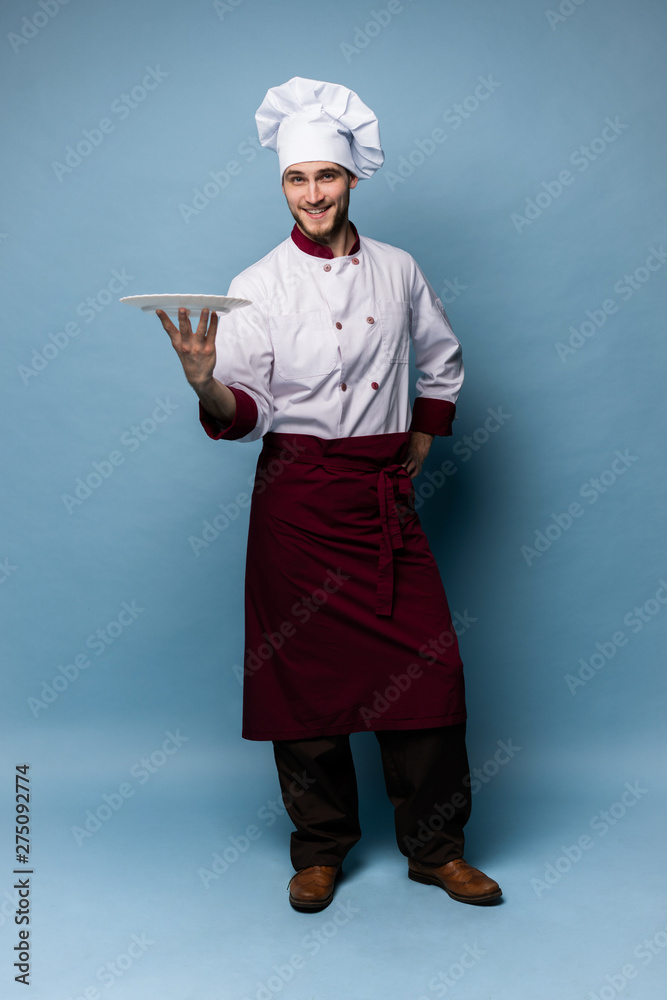 Happy male chef cook standing with plate isolated on light blue background. Happy male chef cook standing with plate isolated on light blue background.