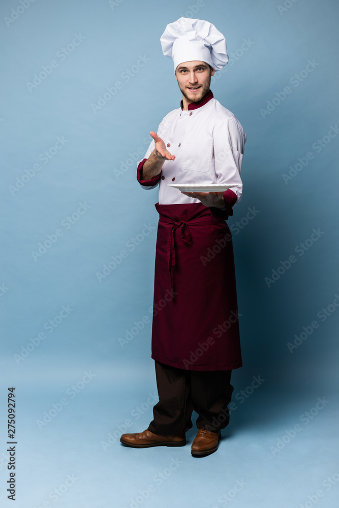 Happy male chef cook standing with plate isolated on light blue background. Happy male chef cook standing with plate isolated on light blue background.