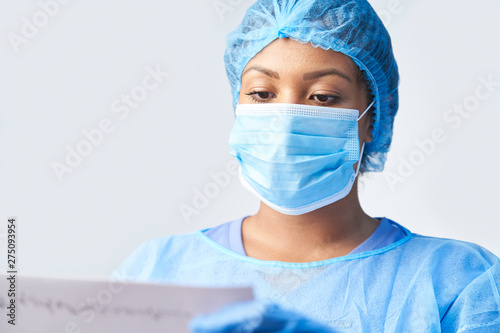 Studio Shot Of Female Surgeon Wearing Gown And Mask Holding Medical Print Out