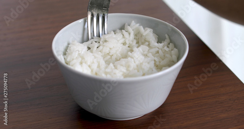Closeup of woman eating rice from bowl with fork