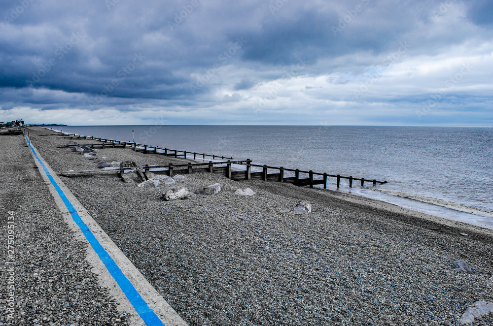 A beach in Suffolk with pebbles and breakwaters with cloudy sky